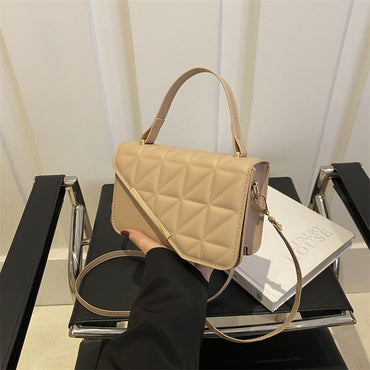 Beige quilted handbag held over a stack of books on a black surface.